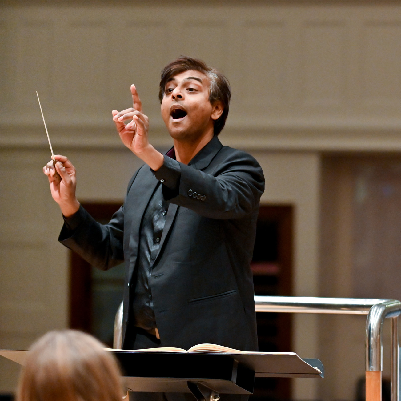 Male student, conducting a rehearsal for an upcoming orchestra, with musicians in the foreground.